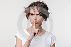 Portrait of angry woman with short brown hair in basic t-shirt holding index finger on lips