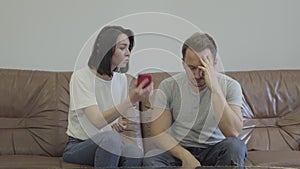 Portrait of angry woman shouting at her sad husband showing cellphone with messages from his paramour at home. Problems