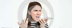 Portrait of angry woman shouting at smartphone speakerphone, recording voice message with annoyed face expression