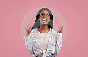 Portrait of angry young black woman screaming on pink studio background