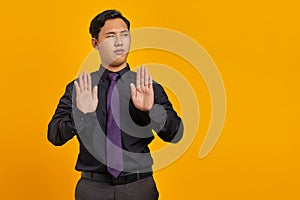 Portrait of angry young handsome businessman doing stop gesture with hand palms on yellow background