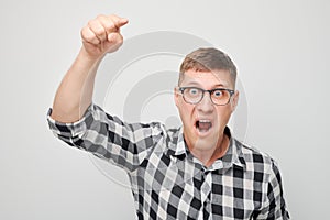 Portrait of angry young man yelling pointing menacingly at camera isolated on white studio background