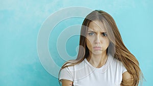 Portrait of angry young woman looking into camera nervous on blue background
