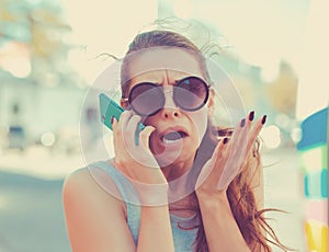 Portrait angry young woman screaming on mobile phone standing outside with city background. Negative emotions feelings