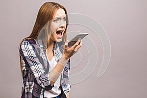 Portrait of an angry young woman shouting at a mobile phone, isolated on a grey background