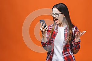 Portrait of an angry young woman shouting at a mobile phone, isolated on a orange background