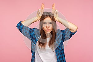 Portrait of angry young woman showing bull horn gesture, looking at camera with hostile menace expression