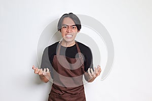 Portrait of annoyed Asian barista man in brown apron making angry hand gesture with fingers