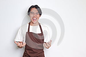 Portrait of annoyed Asian barista man in brown apron making angry hand gesture with fingers