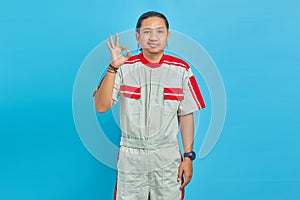Portrait of annoyed handsome man wearing mechanical uniform showing okay gesture forced over blue background