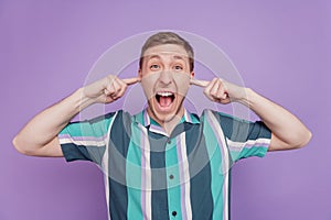 Portrait of annoyed irritated guy fingers close ears open mouth shout loud on purple background