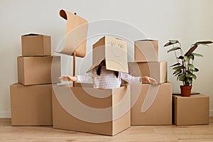 Portrait of anonymous little girl sitting in cardboard ship with sail with carton box with drawn face on her head, spreading hands