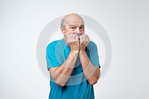 Portrait of anxious senior man in blue t-shirt biting his nails fingers freaking out