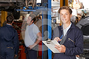 Portrait Of Apprentice Mechanic Holding Clipboard Working In Auto Repair Shop