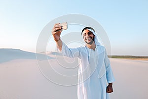 Portrait of Arabian sheikh man with gadget that communicates in skype against blue sky on summer day.