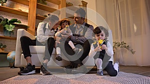 Portrait of arabic father sitting on sofa with his twin sons and teenager and playing with toys in living room.