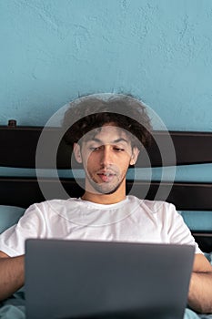 Portrait of arabic guy in weekend morning, working on laptop writing check, wearing nightwear sleep wear t-shirt