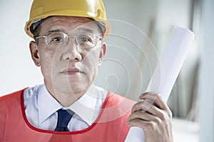 Portrait of architect in a hardhat holding a rolled up blueprint indoors, close-up