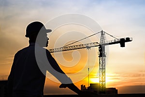 Portrait of architect silhouette wear a helmet at construction site with crane background and sunset