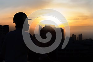 Portrait of architect silhouette wear a helmet at construction site with crane background and sunset