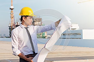 Portrait of architect wear yellow safety helmet and verify the blueprint with commitment on construction site with crane