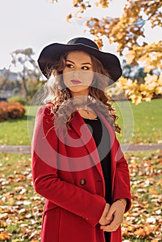 Portrait of an aristocratic girl walking in an autumn park in a red coat and a black hat