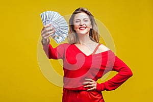 Portrait of arrogant wealthy beautiful woman in red dress holding money, isolated on yellow background