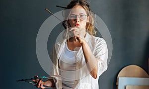 Portrait of an artist female painting something in her art studio. A young woman painter in transparent eyeglasses draws in the