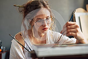 Portrait of an artist female standing next to the easel with canvas painting something in her art studio. A professional young