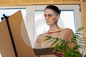 Portrait of an artist at work, a girl draws a drawing on an easel by the window