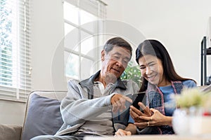 Portrait of Asian adorable senior couple using smartphone together video chatting with family in living room at home.