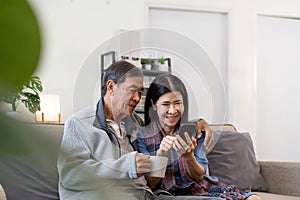 Portrait of Asian adorable senior couple using smartphone together video chatting with family in living room at home.