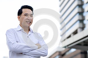 Portrait Asian adult man looks to copy space with arm crossed Confident business man in white shirt He standing outdoor in city