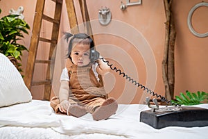 Portrait of asian baby infant playing classic vintage telephone on tropical tree bed. kid sitting on bed. studio shot. baby