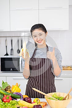 Portrait of asian beautiful woman and housewife is smiling and holding banana in white kitchen. Healthy food concept,Beautiful
