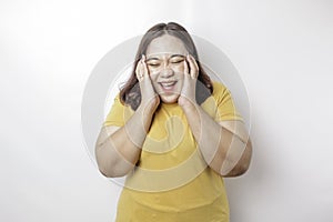 A portrait of an Asian big sized woman wearing a yellow t-shirt isolated by white background looks depressed