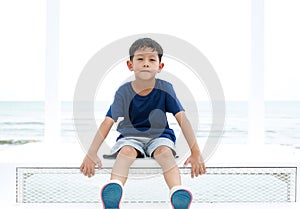 Portrait of Asian boy child looking camera with smiling while sitting on white stair at seaside