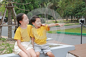 Portrait of Asian boy and girl are sitting in the park and pointing at something beside them, Children are friends in the garden