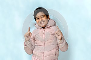 portrait of an Asian boy wearing winter clothes with smile and point up expressions, against a white background.