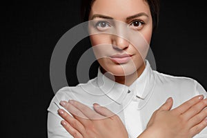 Portrait of Asian brunette woman in white shirt with arms crossed on chest on black background