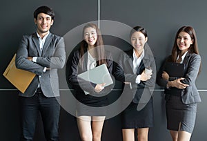 Portrait of Asian business people posing in office building. Young businessman and businesswoman leaning against the wall.