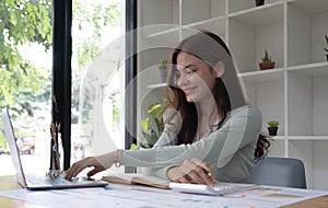 Portrait of asian business woman paying bills online with laptop in office. Beautiful girl with computer and chequebook