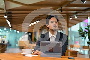 Portrait of Asian businessman in coffee shop thinking and using digital tablet computer