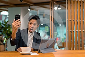 Portrait of Asian businessman in coffee shop using digital tablet computer and mobile phone