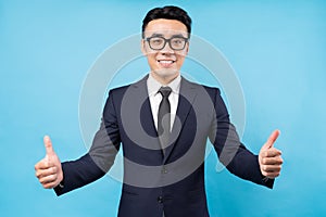 Portrait of asian businessman giving thumbs up on blue background