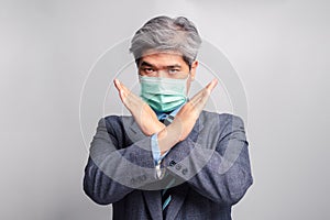 Portrait of Asian businessman with surgical medical mask looking at camera and Raise your hand forbid. Concept of prevent
