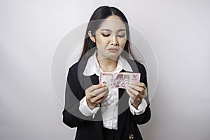 A portrait of an Asian businesswoman wearing a black suit and holding money in Indonesian Rupiah isolated by white background
