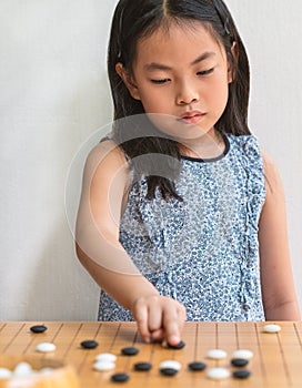 Portrait Asian child girl plays Go, the Japanese board game or Chinese board game, focus on the board game, white wall, vertical