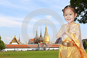 Portrait of asian child girl in traditional thai dress praying against Grand palace and Wat Phra Keaw