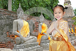 Portrait of asian child girl in traditional thai dress praying against old buddha statue at ayutthaya in thailand